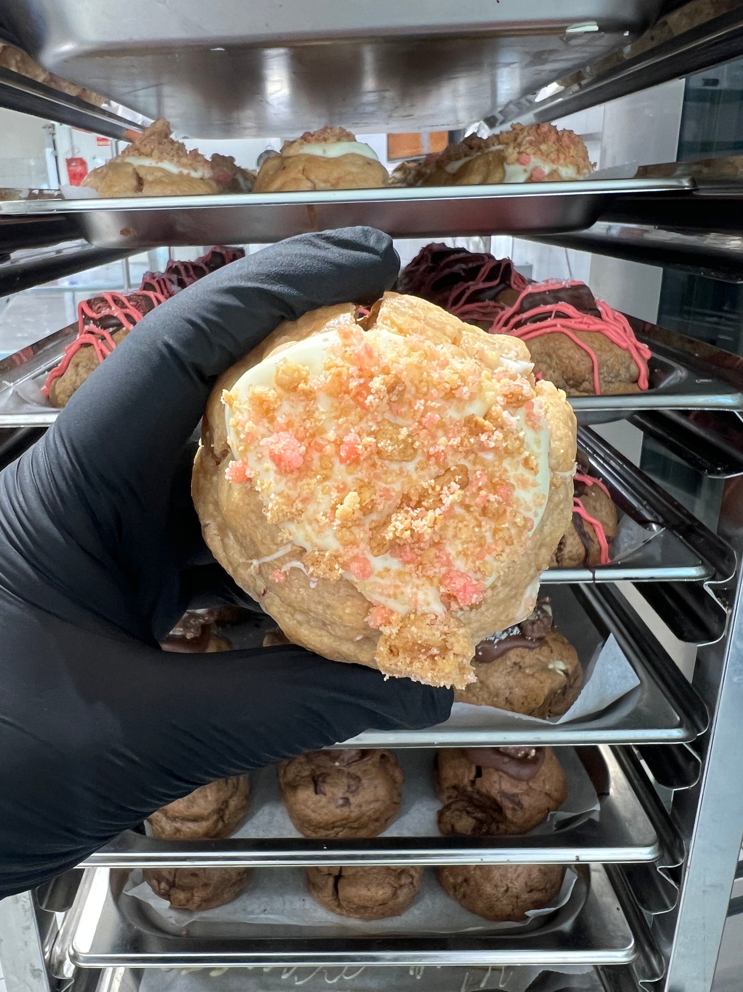 Top view of our Strawberry Shortcake Loaded Cookie, showcasing the white chocolate drizzle, strawberry crumble, and cheesecake frosting peeking through.